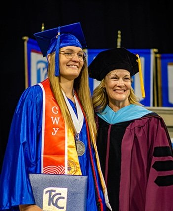 TCC Graduate Kelly Parsley, Stands in her cap and gown with tcc administrator at graduation.