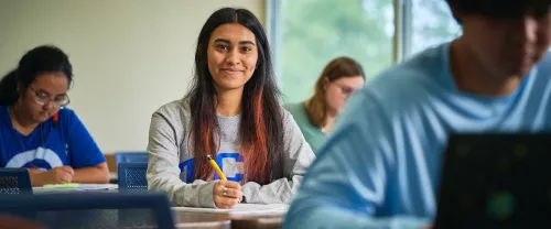 Female TCC Student smiles at you will she sits in class and takes notes.