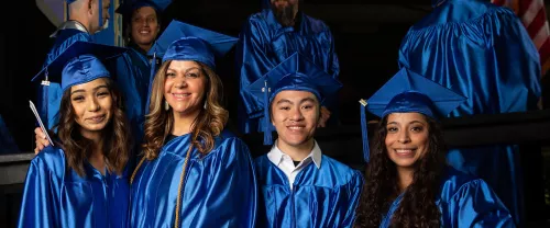 Four TCC Graduates Stand together in blue caps and gowns. 