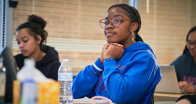 Young black female TCC Student sits thoughtfully in class with hands folded under her chin.