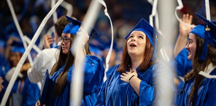TCC Graduate smiles and looks up at falling white streamers.