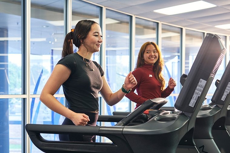 Two female TCC students jog on treadmills at the Southeast Campus fitness center.