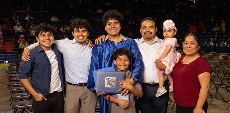 TCC graduate in blue graduation gown poses with 6 family members.