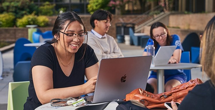 Young TCC student works on her lap top at a table outside on the Southeast Campus.